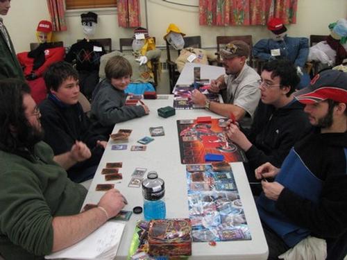 A past Yu-Gi_Oh program. - Yu-Gi-Oh players strategize while scarwcrows look on.