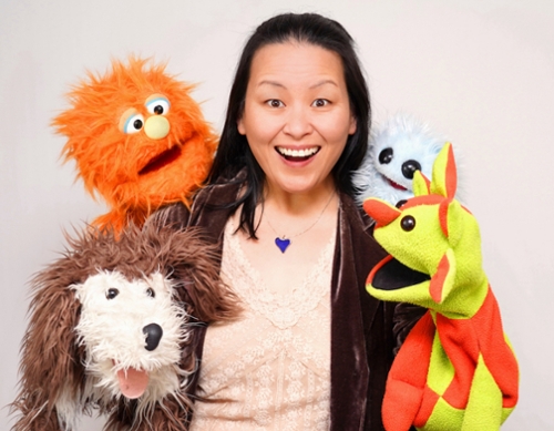 Four colorful puppets around a smiling woman with dark hair.