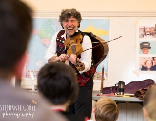 A man with grey fluffy hair and a big smile playing a string instrument.