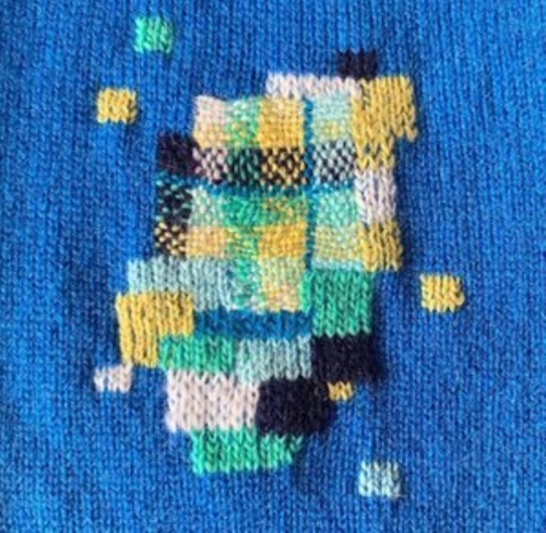 Example of an artful stick that is blue, teal, white, and pastel yellow squares on a blue stitched fabric.