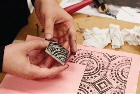 A hand with a stamp and an example of block printing in front of that.